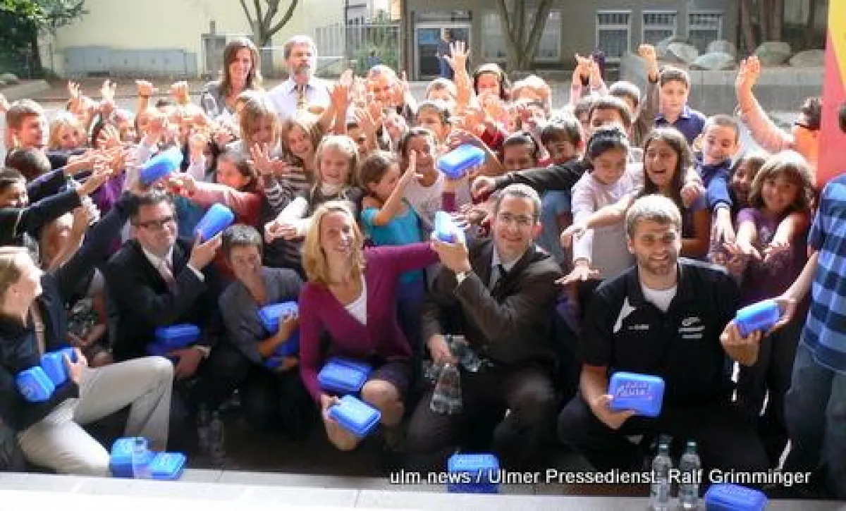 Die Göppinger Grundschüler mit Handballstar Michael Schweikardt (re) und den Sponsoren der Schulaktion Gesunde Pause bei der Übergabe der Vesperboxen im Pausenhof.