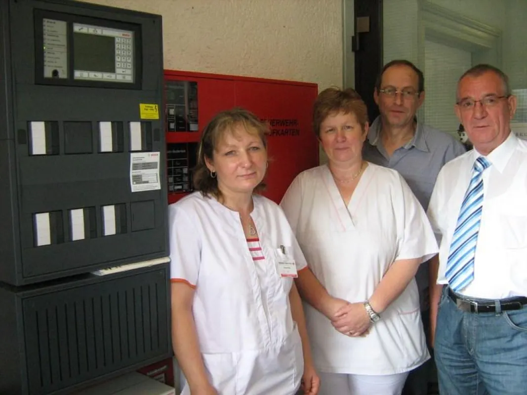 Pflegepersonal, Heimleitung und Geschäftsführer vor der neuen Brandmeldeanlage