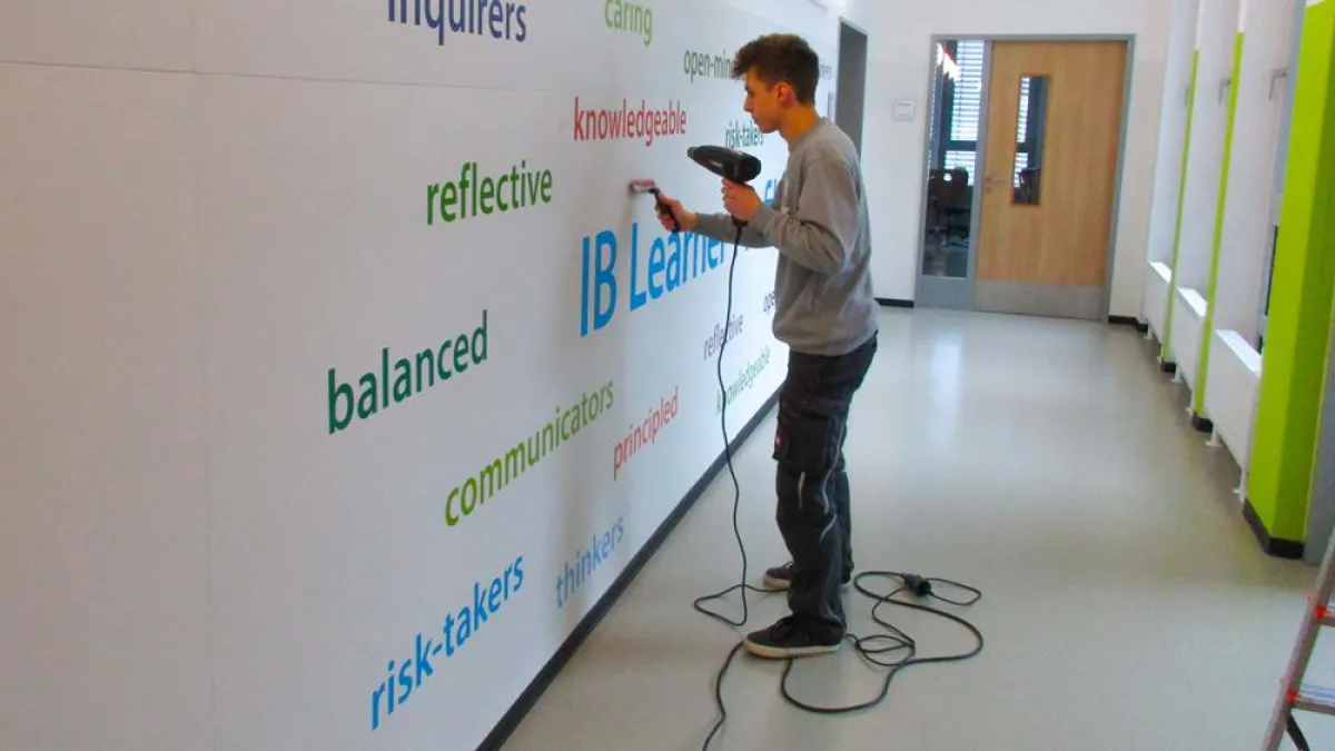 Werbetechniker bringt in der Bonn International School e.V. ein Wandtattoo an.