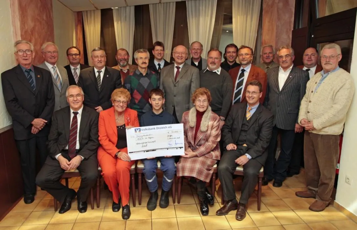 große Scheckübergabe: vorne sitzend links: Helmut Hoffmann, Vorstand; vorne sitzend rechts: Stephan M. Schader, Vorstandsvorsitzender; stehend in der Mitte: Langens Bürgermeister Frieder Gebhardt