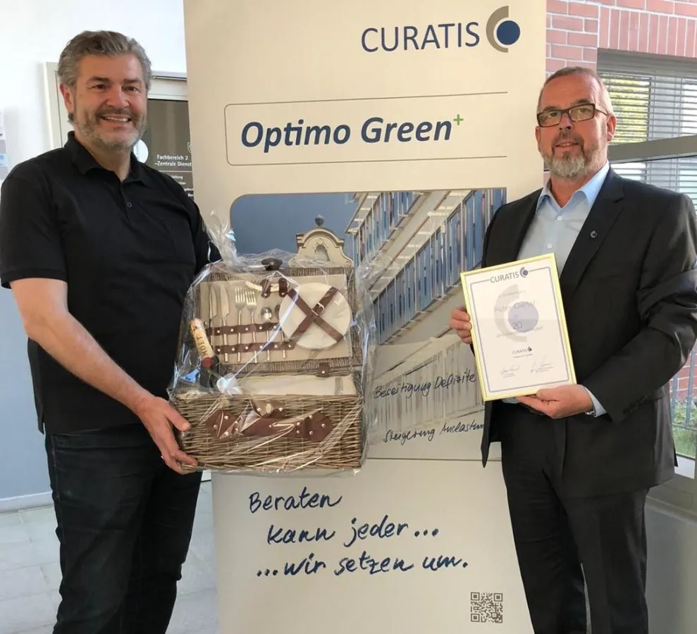 Bildtext: CURATIS-Chef Franz Kissel überreicht Peter Oertel einen Geschenkkorb zum 20. Jubiläum (Fot