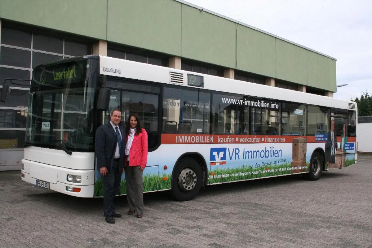 Die Immobilienvermittler Frau Petra Röll und Herr Hagen Busch vor dem neu beschrifteten Bus.