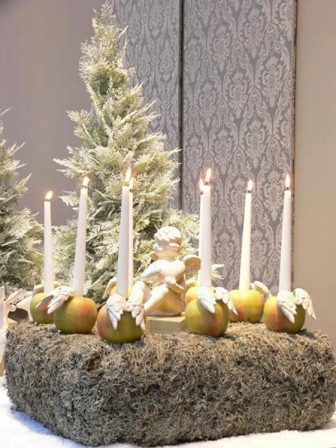 Knackige Äpfel, dekoriert mit hübschen Porzellanflügeln, dienen hier als Kerzenhalter. Die weißen Leuchterkerzen mit dem RAL-Gütezeichen wirken so auf dem Kranz neu & originell! Fotovermerk: Gütegemei