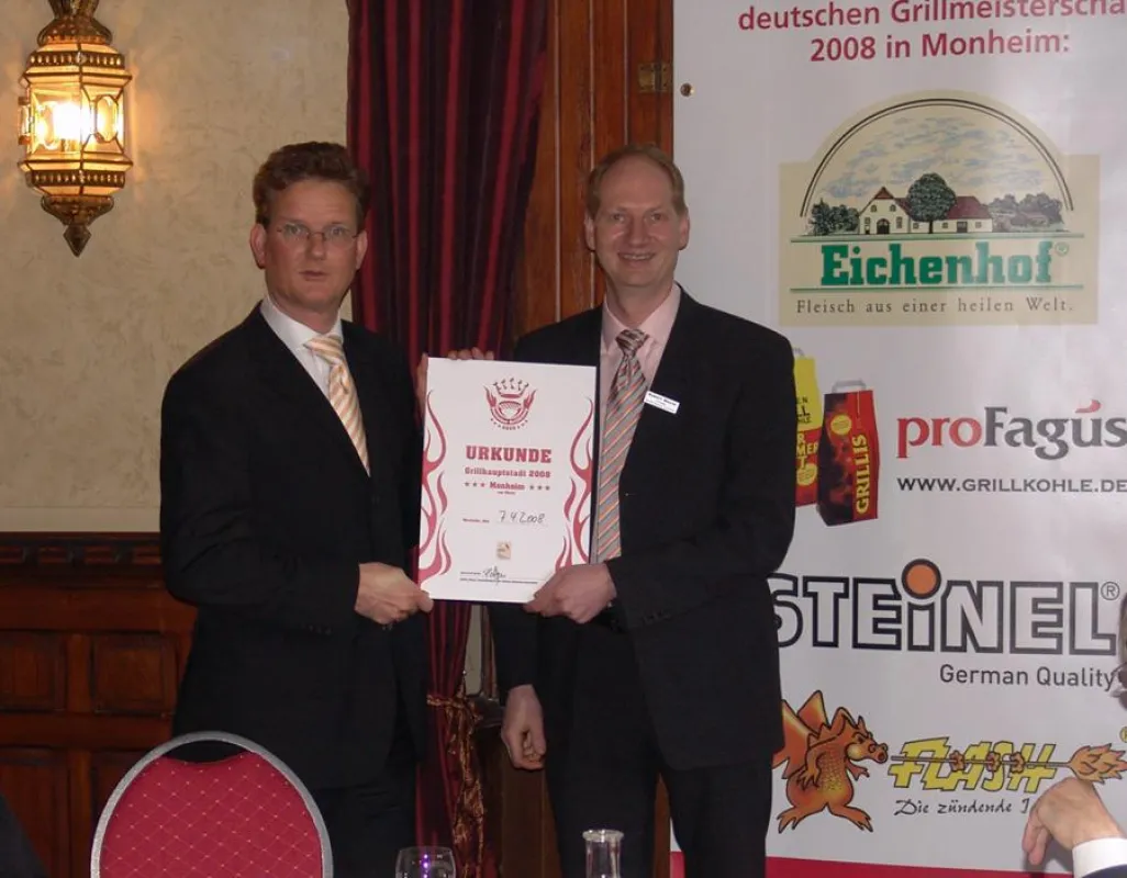 von links nach rechts: Dr. Thomas Dünchheim, Bürgermeister der Stadt Monheim, erhält die Ernennungsurkunde zur Grillhauptstadt von Robert Meyer, Präsident GBA.