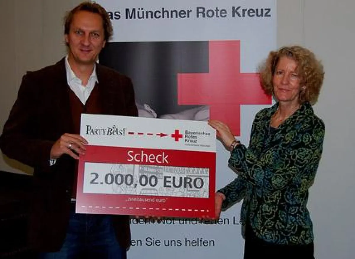 Marion Ivakko, stellvertretende Geschäftsführerin des BRK-Kreisverbandes München, freut sich über den Spendenscheck von PartyBets, der von Christian Prechtl von der betreuenden Agentur Feuerstein PR &
