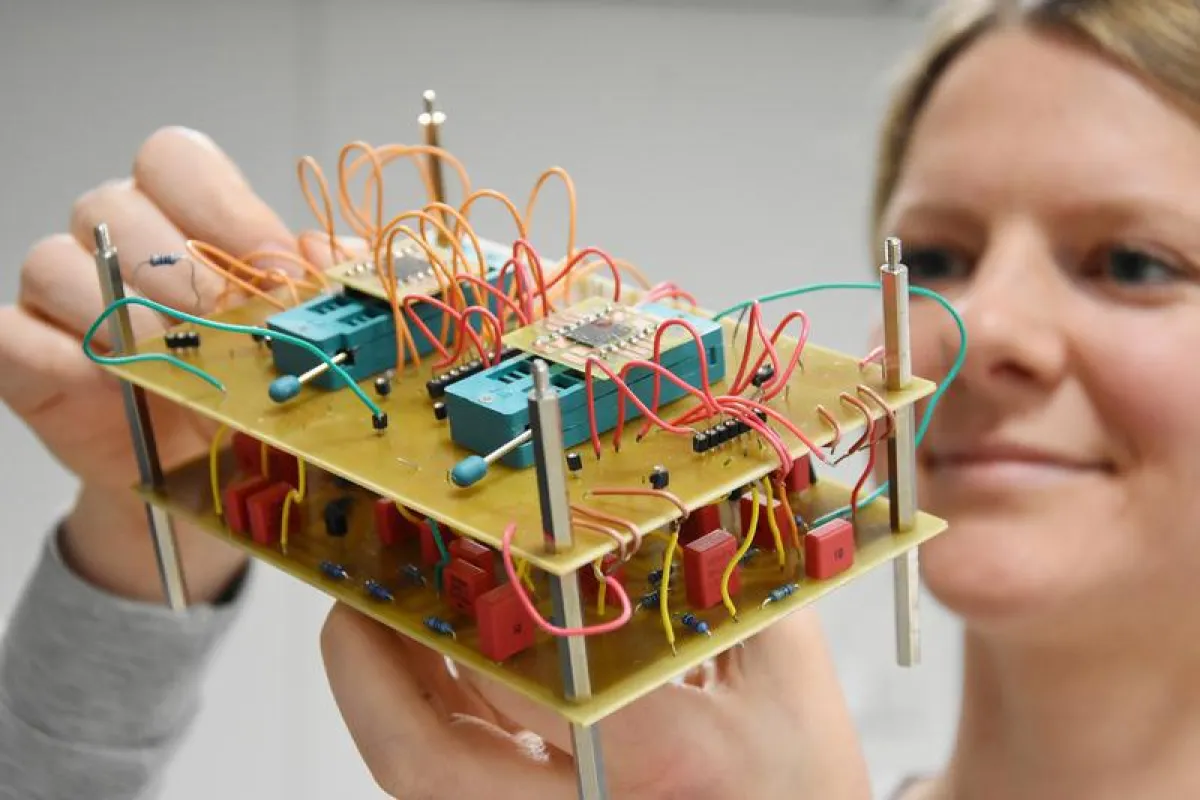 Marina Ignatov, Doktorandin der Elektrotechnik und Erstautorin der Publikation, zeigt eine elektronische Schaltung, mit der Wahrnehmungsprozesse des menschlichen Gehirns nachgebildet werden können.  (