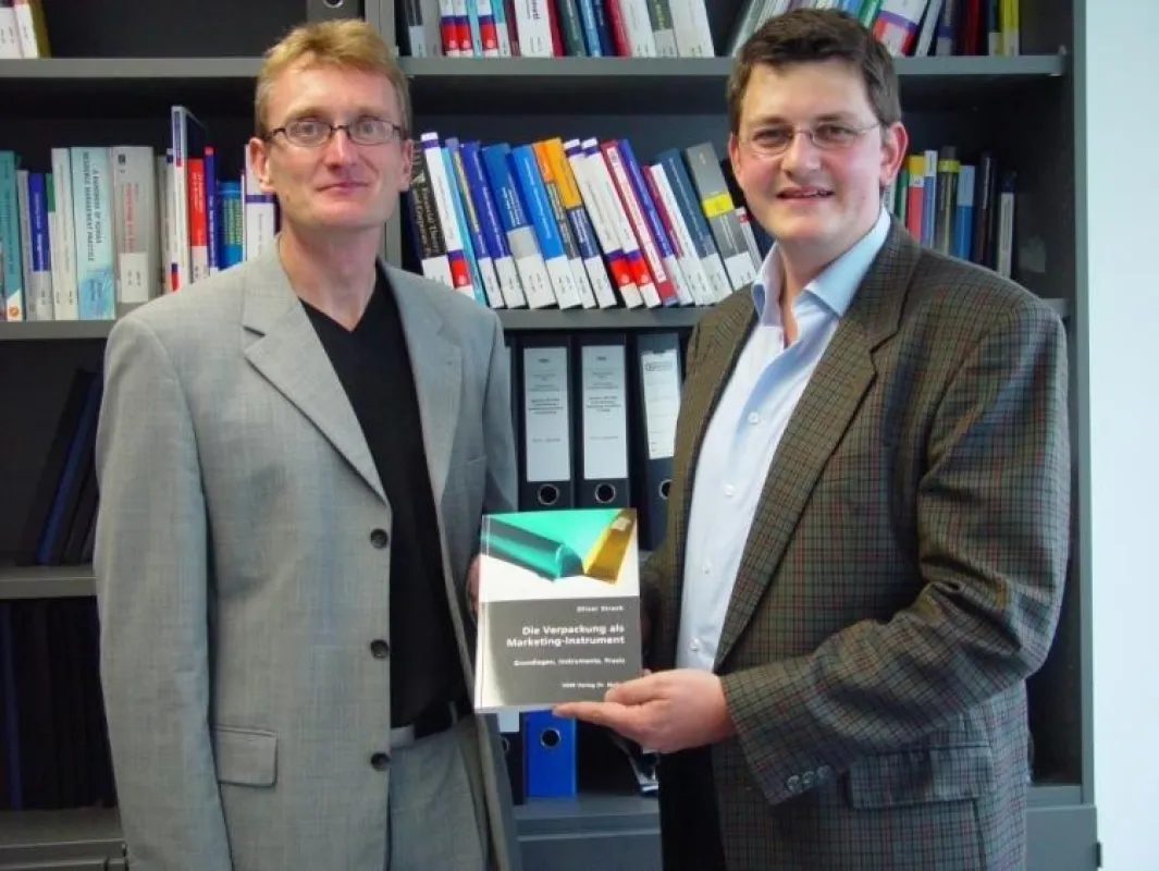 Autor Oliver Strack (rechts) übergibt Fachbuch an Prof. Dr. Alexander Haubrock von der HTW Aalen