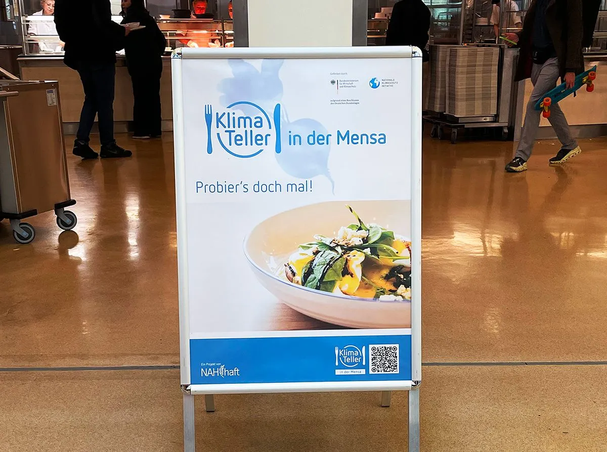 Ein Poster lädt ein, die KlimaTeller Gerichte in der Mensa zu probieren.