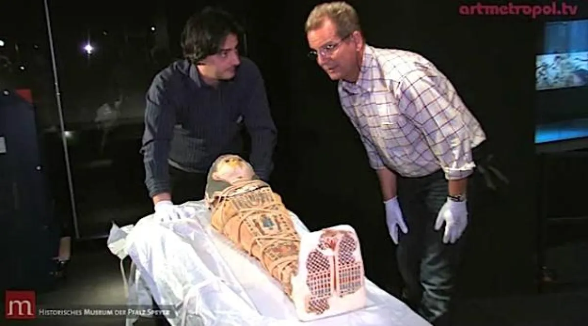 Restaurator Lucius Alsen (re.) bringt eine Kindermumie in die Vitrine ein.