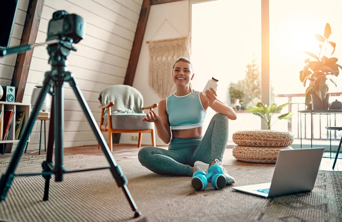 Woman blogger in sportswear sitting on the floor with dumbbells and a laptop (© Adobe Stock/Valerii Apetroaiei #327395794)