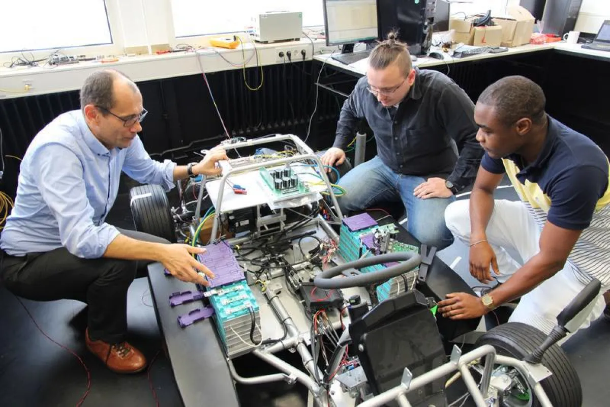 Prof. Alexander Kuznietsov, Tilman Happek und Frank Tanenkeu (von links) arbeiten am hochschuleigenen Elektrofahrzeug, in dem das Batteriemanagementsystem getestet wird. (THM/Armin Eikenberg)