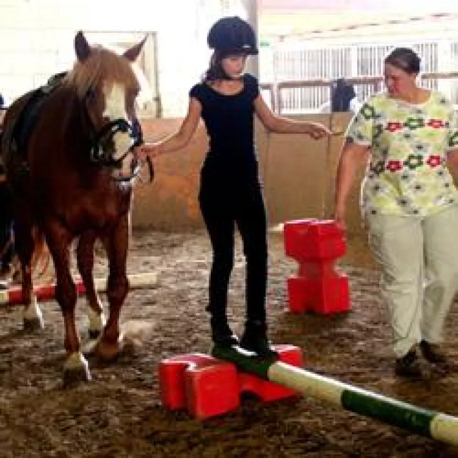 Anna-Marie Bartsch balanciert mit einer Kartoffel auf einem Löffel über eine Stange und führt dabei Schulpferd Ronja - Übungsleiterin Martina Oribold passt auf, dass alles ordnungsgemäß abläuft