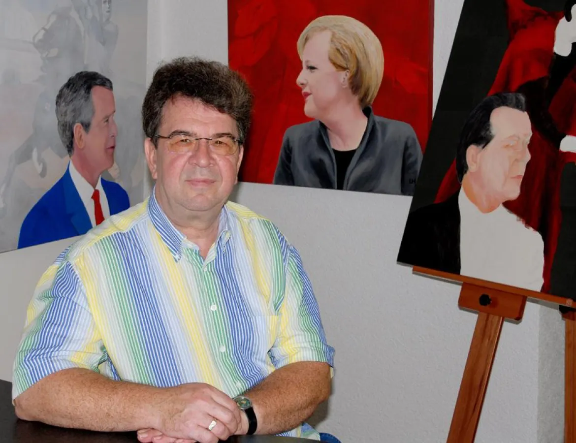 Udo A. Heinrich vor den Bildern der Serie \'Profile und Verbindungen\' mit Angela Merkel, Franz Müntefering und George W. Bush
