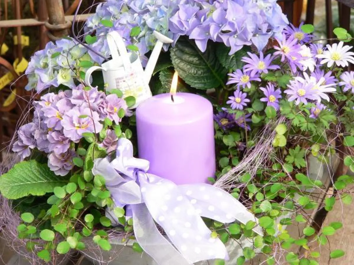 Die fliederfarbene Stumpenkerze passt perfekt zu den Blüten des Blumengestecks - ein tolles Highlight!Foto:Gütegemeinschaft Kerzen