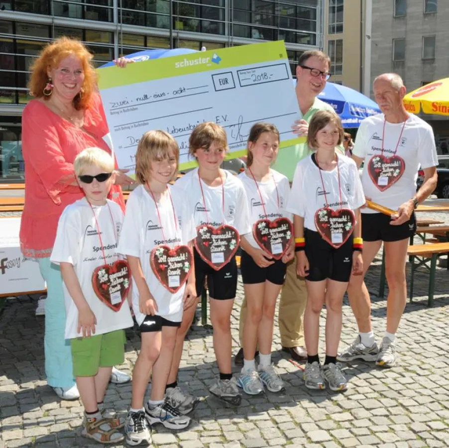 Scheckübergabe von Florian Schuster an Petra Windisch mit Läufern der Aktion 