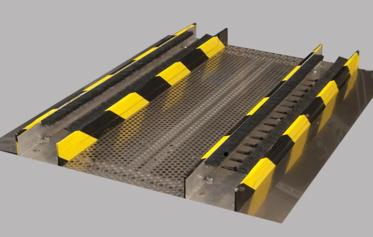 Die Räder eines Transportwagens durchlaufen die Reinigungsschienen und werden durch seitlich angebrachte Bürsten und rotierende Borsten von unten gereinigt