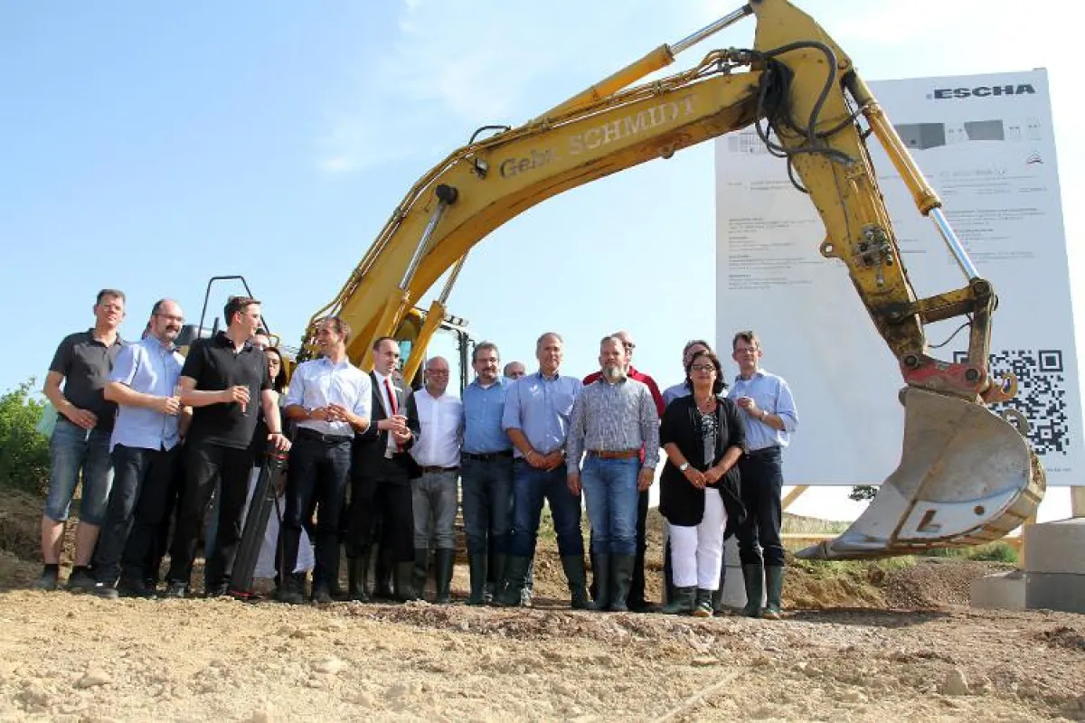 Gäste und Mitarbeiter begehen den Spatenstich mit einem Bagger anstelle eines klassischen Spatens