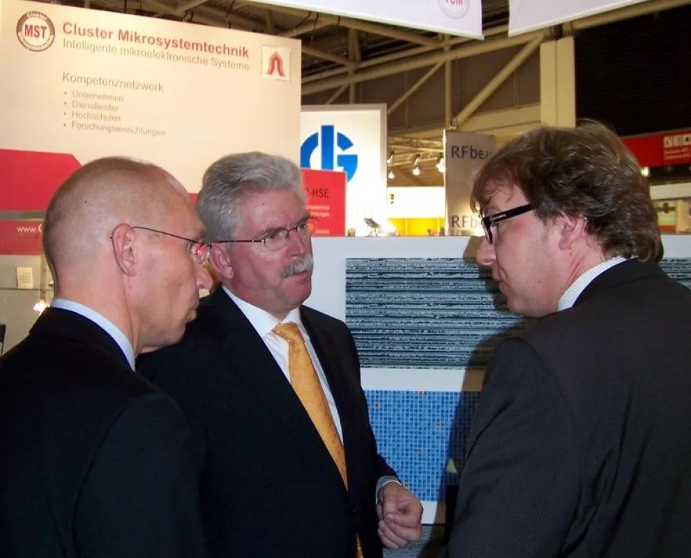 Der Bayerische Wirtschaftsminister Manfred Zeil (Bildmitte) informiert sich am Gemeinschaftsstand des Clusters Mikrosystemtechnik bei Günther Irlbacher (rechts) über die integrierten Glas-Bedienoberfl