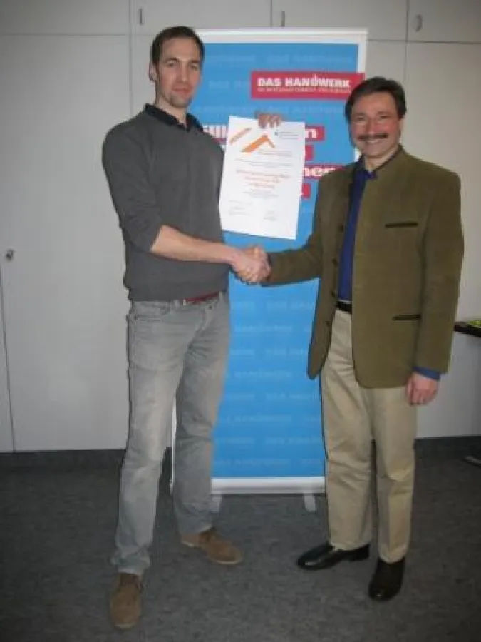 Der Leiter des BBZ überreicht die Urkunde an Herrn Heinrich, Mitarbeiter der Schreinerei Mayr (v.r.)