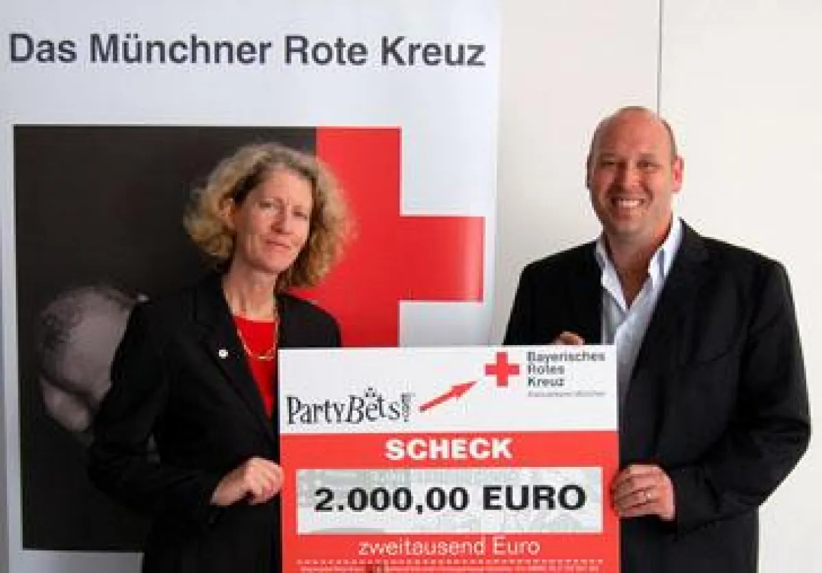 Marion Ivakko, stellvertretende Geschäftsführerin des BRK-Kreisverbandes München, freut sich über den Spendenscheck von PartyBets, der von Felix Feuerstein überreicht wird.